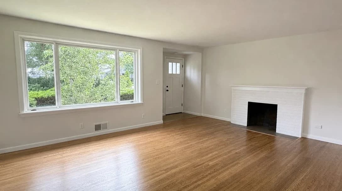 Empty living room with bare walls, hardwood floor, and natural light
